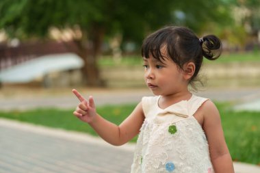 Küçük kız parkta bir şey gösteriyor.