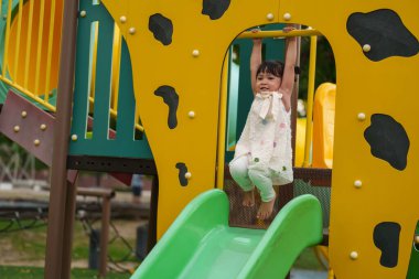 Parktaki çocuk parkında sarı barı elinden tutan mutlu küçük kız.