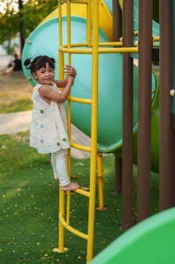 Parktaki çocuk parkında oynayan ve tırmanan mutlu kız.