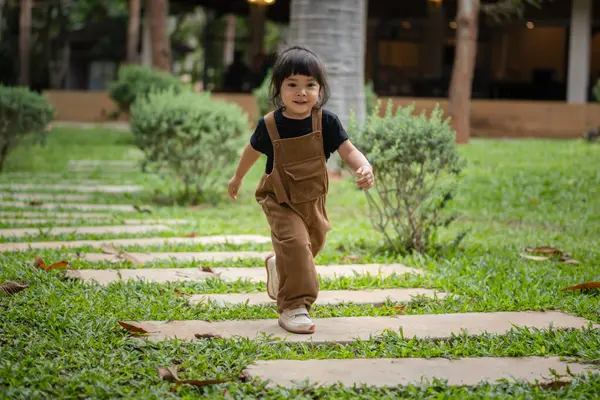 Mutlu küçük kız bahçede taş bir yolda yürüyor.