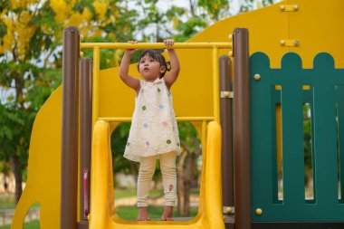 Parktaki çocuk parkında sarı barı elinden tutan mutlu küçük kız.