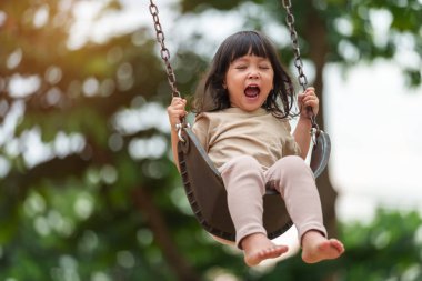 Neşeli küçük kız dışarıda salıncakta sallanıyor.