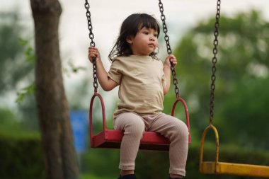 Neşeli küçük kız dışarıda salıncakta sallanıyor.