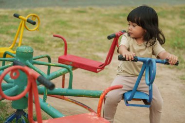 Küçük kız dışarıda oyun bahçesinde atlıkarıncada oynarken eğleniyor.