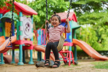 Neşeli küçük kız dışarıda salıncakta sallanıyor.