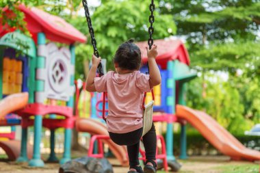 Neşeli küçük kız dışarıda salıncakta sallanıyor.