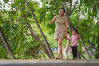 Yürüyen ve parktaki kaldırımda annesiyle el ele tutuşan küçük bir kız.