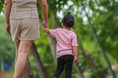 Yürüyen ve parktaki kaldırımda annesiyle el ele tutuşan küçük bir kız.