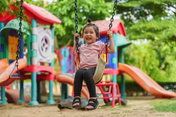 Neşeli küçük kız dışarıda salıncakta sallanıyor.