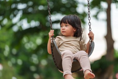 Neşeli küçük kız dışarıda salıncakta sallanıyor.