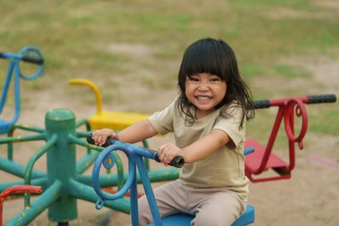 Küçük kız dışarıda oyun bahçesinde atlıkarıncada oynarken eğleniyor.