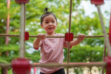 Parktaki çocuk parkında tırmanma halatlarıyla oynayan mutlu bir kız.