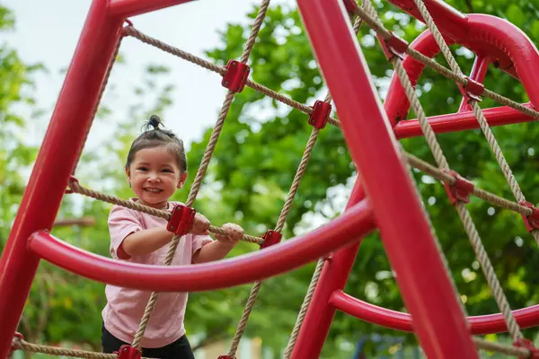 Parktaki çocuk parkında tırmanma halatlarıyla oynayan mutlu bir kız.