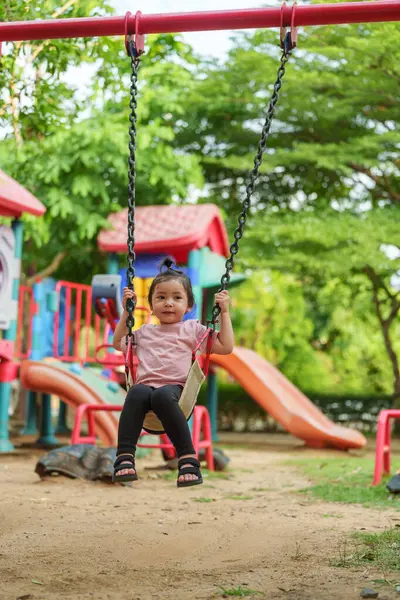 Neşeli küçük kız dışarıda salıncakta sallanıyor.