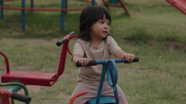 Küçük kız dışarıda oyun bahçesinde atlıkarıncada oynarken eğleniyor.