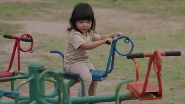 Küçük kız dışarıda oyun bahçesinde atlıkarıncada oynarken eğleniyor.