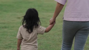 Yürüyen küçük kız çimenlikte annesiyle el ele tutuşuyor.