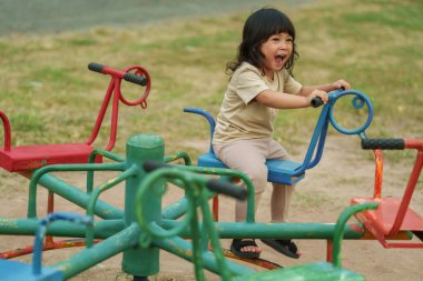 Küçük kız dışarıda oyun bahçesinde atlıkarıncada oynarken eğleniyor.