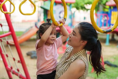 Anne kızını oyun sahasındaki yüzüklere asmak için tutuyor.