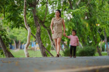 Yürüyen ve parktaki kaldırımda annesiyle el ele tutuşan küçük bir kız.