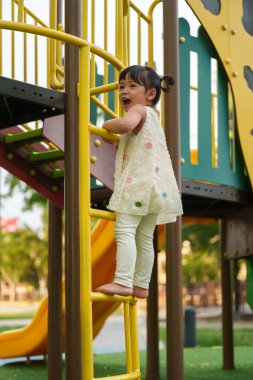Parktaki çocuk parkında oynayan ve tırmanan mutlu kız.