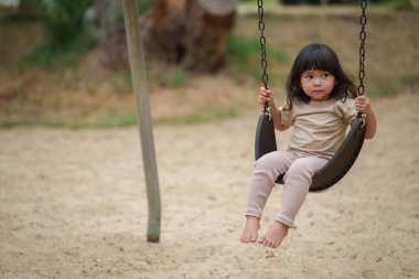 Neşeli küçük kız dışarıda salıncakta sallanıyor.