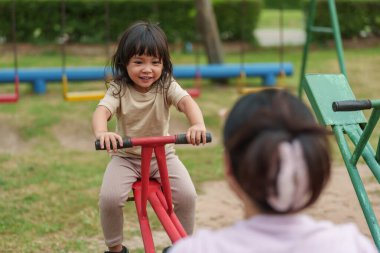 Küçük kız ve anne bahçede tahterevalli oynuyorlar.