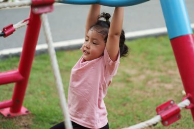Parktaki çocuk parkında barın önünde elini sallayan küçük mutlu kız.