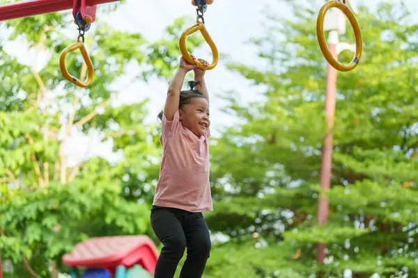 Parkta çocuk parkındaki yüzüklerde asılı duran küçük kız.