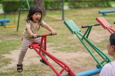 Küçük kız ve anne bahçede tahterevalli oynuyorlar.