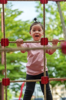 Parktaki çocuk parkında tırmanma halatlarıyla oynayan mutlu bir kız.