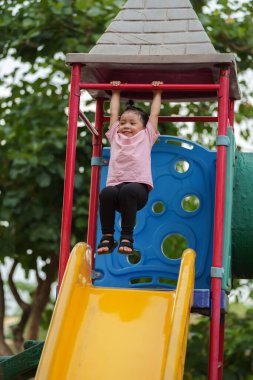 Parktaki çocuk parkında kırmızı çubuğu elinde sallayan küçük mutlu kız.