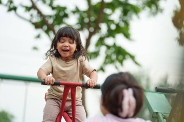 Küçük kız ve anne bahçede tahterevalli oynuyorlar.