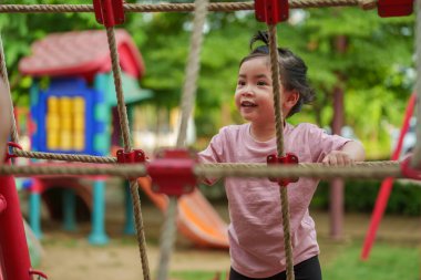 Parktaki çocuk parkında tırmanma halatlarıyla oynayan mutlu bir kız.