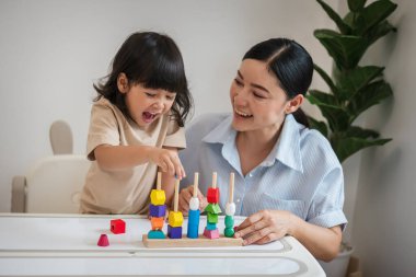 Küçük kız ve annesi evde eğitici tahta oyuncaklarla oynuyorlar.