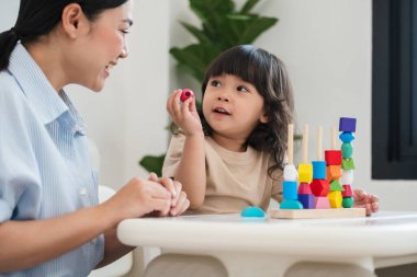 Küçük kız ve annesi evde eğitici tahta oyuncaklarla oynuyorlar.