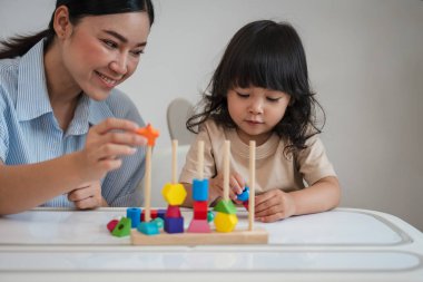 Küçük kız ve annesi evde eğitici tahta oyuncaklarla oynuyorlar.