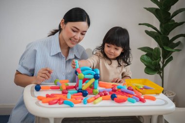 Küçük kız ve annesi evde renkli manyetik inşaat oyuncağı oynuyorlar.
