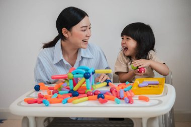 Küçük kız ve annesi evde renkli manyetik inşaat oyuncağı oynuyorlar.
