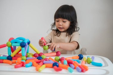 Küçük kız evde renkli manyetik inşaat oyuncağı oynuyor.