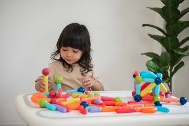 Küçük kız evde renkli manyetik inşaat oyuncağı oynuyor.