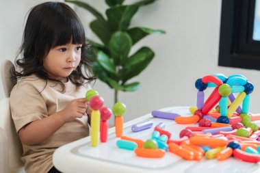 Küçük kız evde renkli manyetik inşaat oyuncağı oynuyor.