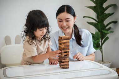 Küçük kız annesiyle birlikte tahta blok oyuncağı oynuyor.