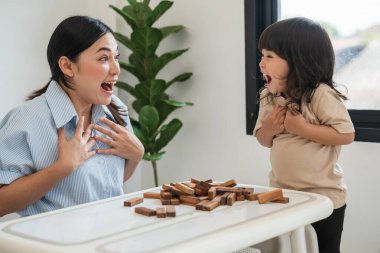 Küçük kız annesiyle birlikte tahta blok oyuncağı oynuyor ve kule çökmesiyle şok oluyor.