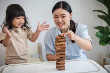 Küçük kız annesiyle birlikte tahta blok oyuncağı oynuyor.