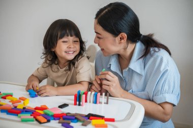 Küçük kız ve annesi renkli tahta blok oyuncakları ya da domino oyunu oynuyorlar.
