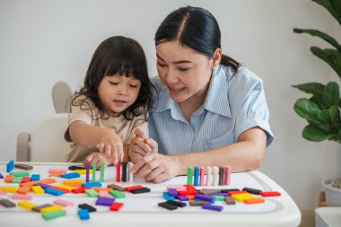 Küçük kız ve annesi renkli tahta blok oyuncakları ya da domino oyunu oynuyorlar.