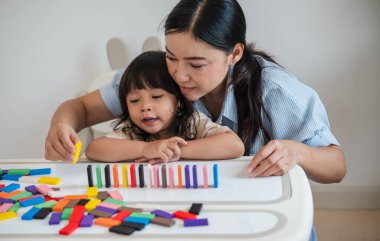 Küçük kız ve annesi renkli tahta blok oyuncakları ya da domino oyunu oynuyorlar.