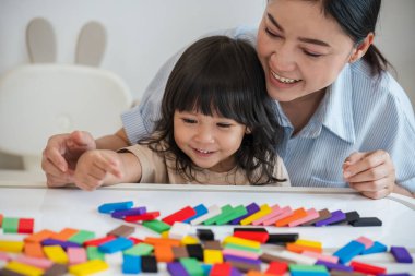 Küçük kız ve annesi renkli tahta blok oyuncakları ya da domino oyunu oynuyorlar.
