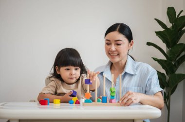 Küçük kız ve annesi evde eğitici tahta oyuncaklarla oynuyorlar.